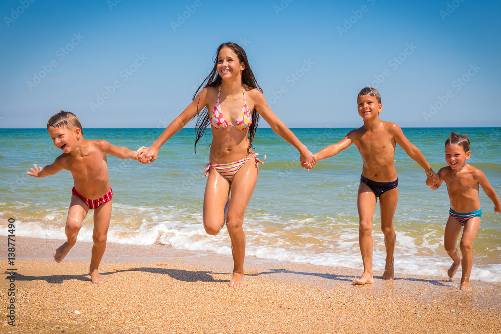 Four kids running from blue sea on sand beach