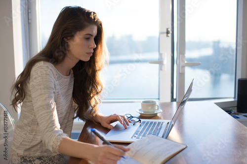 Young woman sits at her laptop with her day planner