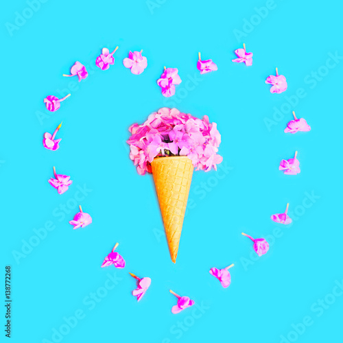 Heart shape of petals with ice cream cone with flowers over colorful blue background