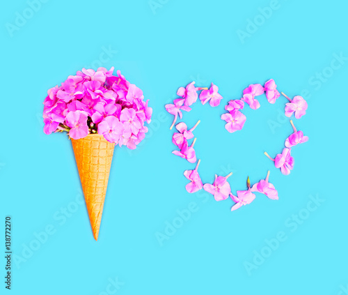Ice cream cone with flowers and heart shape of petals over blue background top view