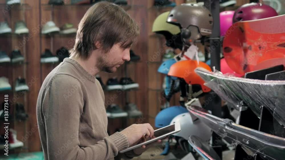 Man consultant check a new snowboard in extreme sport store with tablet pc, deck for rent Man consultant check a new snowboard in extreme sport store with tablet pc, deck for rent