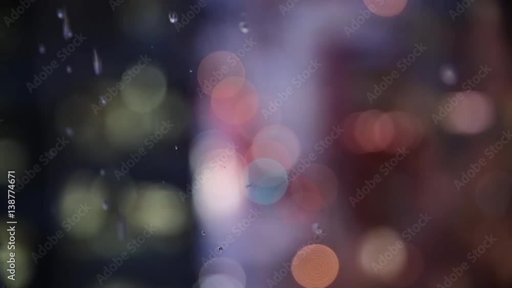 Rain drips down the window of a high rise building in a city. Shallow depth of field with bokeh