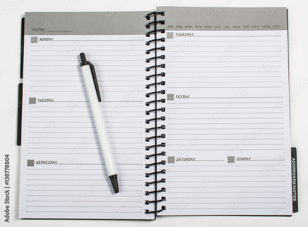 Weekly planner opened with a pen laying on it Weekly planner opened with a pen laying on it