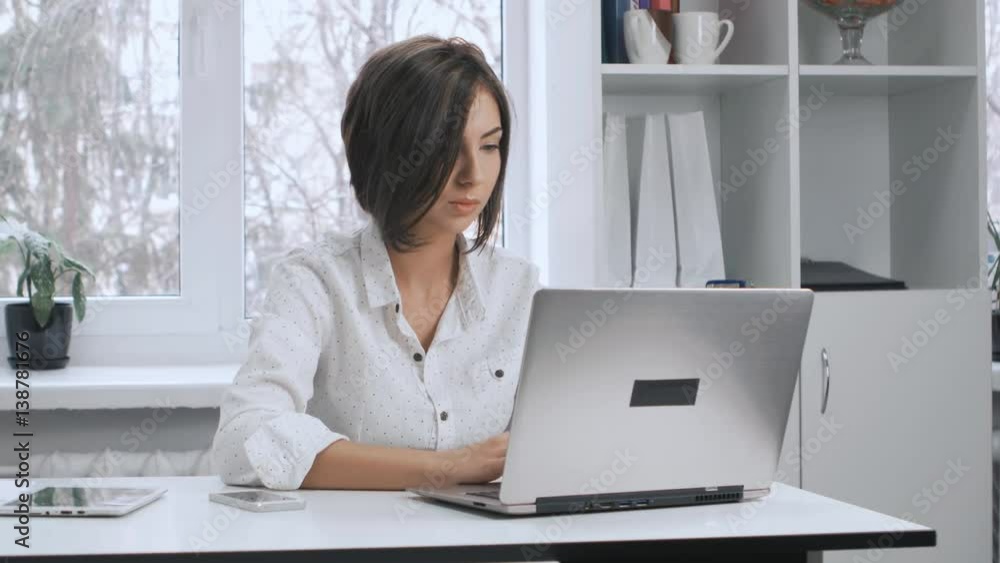 Pretty secretary in white shirt works at a laptop in the office Pretty secretary in white shirt works at a laptop in the office