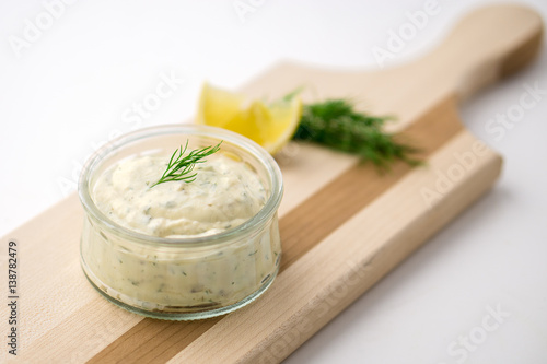 Tartar sauce on a wooden serving board. Made of fresh mayonnaise, lemon and various herbs. This classic creamy sauce is delicious with deep fried fish, seafood and many other dishes.