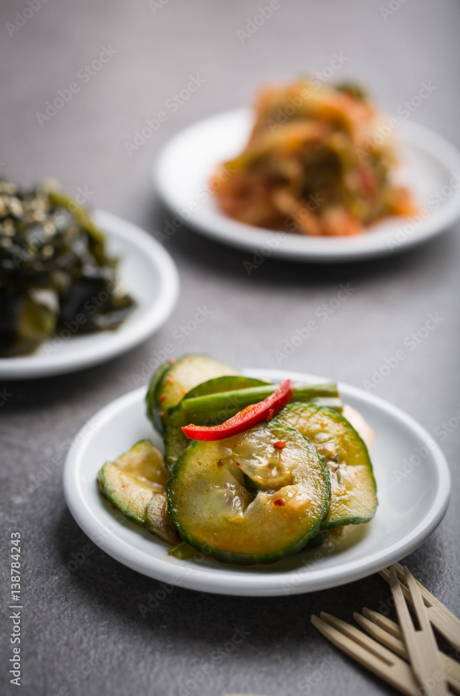 Korean cucumber kimchi on a white dish, More kimchi in the background. Korean cucumber kimchi on a white dish, More kimchi in the background.