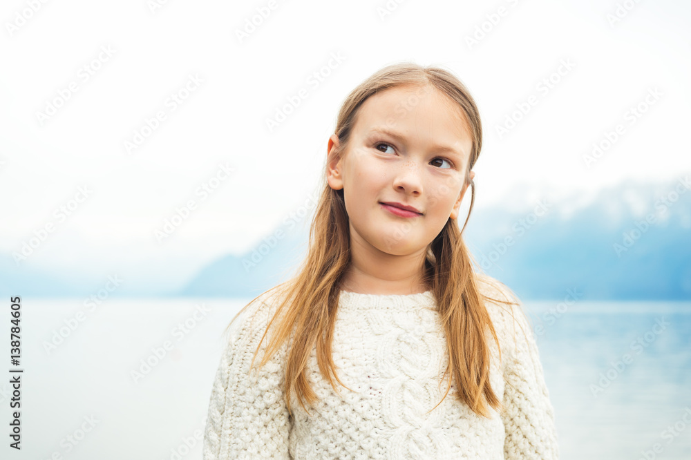 Cute little 8 year old girl playing by the lake on a very windy day, wearing warm white knitted pullover, high key image Cute little 8 year old girl playing by the lake on a very windy day, wearing warm white knitted pullover, high key image