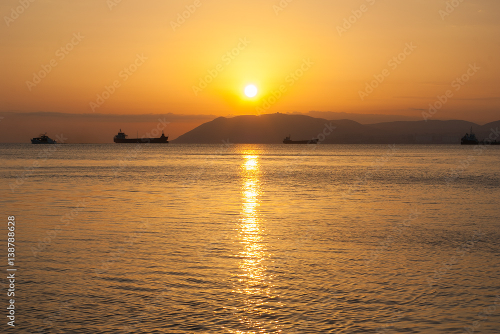 Natural summer sea sunset. Silhouettes of ships and strip of land on the horizon. Orange sea sunset in evening