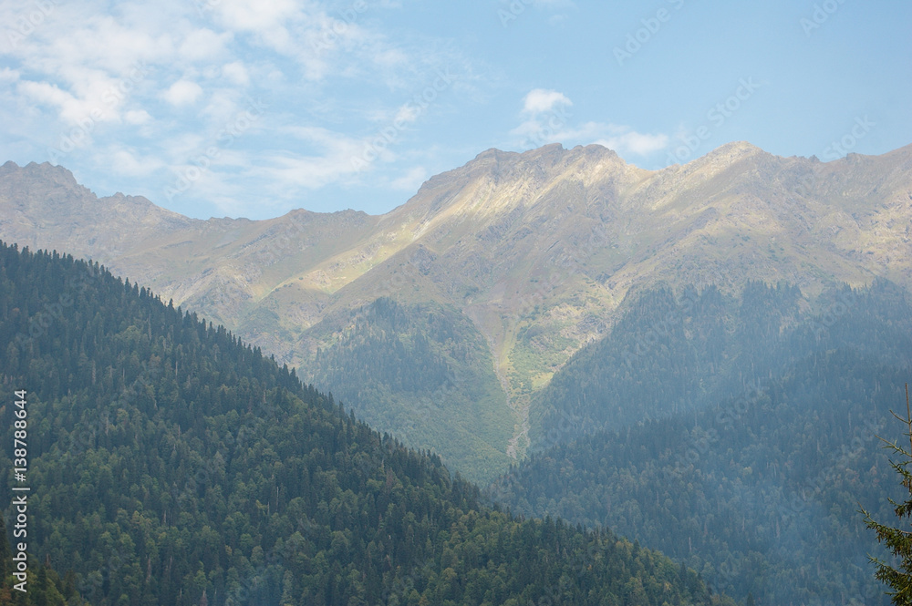 Mountain landscape with blue sky and white clouds. Great nature scenery of green and gray mountain range with sunlight at the middle of summer day.
