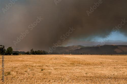 Farm fiels with background of thick black smoke from wildfire © kiravolkov