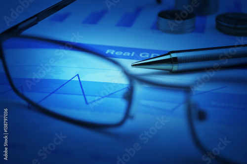Pen and glasses on financial graph and chart, blue tone, Business success concept