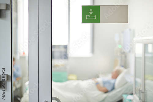 Obraz na płótnie Hospital ward sign on closed glass door in clinic with blurred shape of senior p