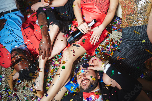 Sticker Tipsy multiethnic group of friends relaxing on floor with colorful confetti whil