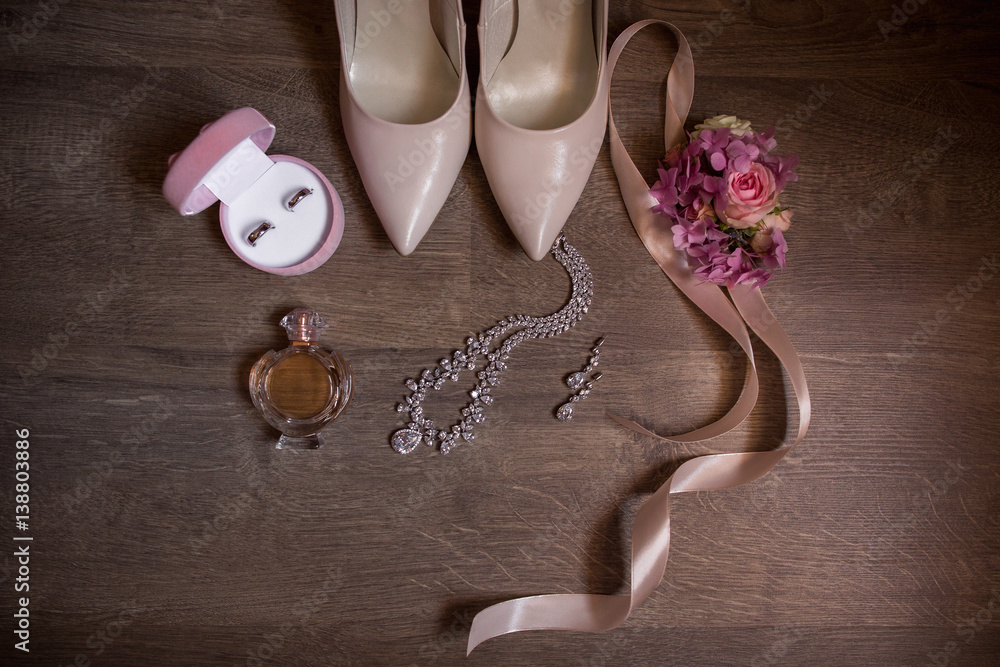 Best wedding accessories on wooden background. Bridal shoes with high heels wedding rings in pink box jewelry perfume bottle and flowers with peach ribbon ideal details for beautiful bride foto de