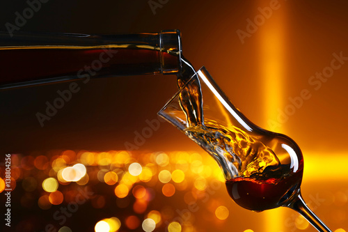 Fotografie Pouring alcohol into a glass on on the background of night city