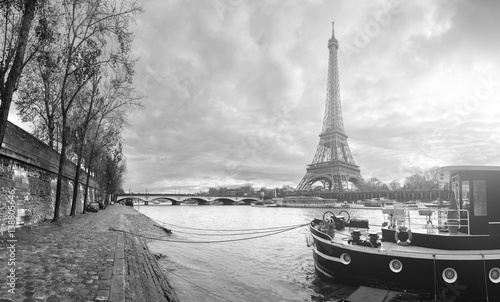 Beautiful panoramic view of the Eiffel Tower and Jena bridge from the river Seine embankment. Dramatic cloudscape. Traditional citycape in backlit morning sunbeam. BW photography. Paris, France.