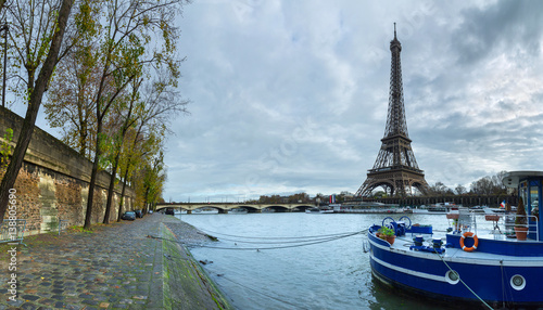 Panoramic view of the Eiffel Tower and Jena bridge from the river Seine embankment. Dramatic cloudscape. Paris, France.