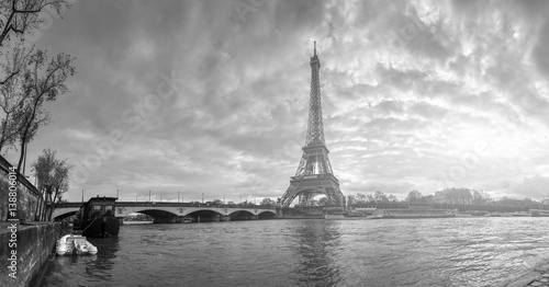 Beautiful panoramic view of the Eiffel Tower and Jena bridge from the river Seine embankment. Dramatic cloudscape. Traditional sitycape in backlit morning sunbeam. BW photography. Paris, France.