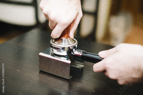 man using a tamper to press freshly ground coffee into a tablet