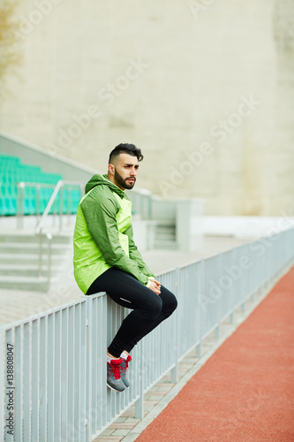 Young fashionable man sitting, resting on railings after running practice in stadium © pressmaster