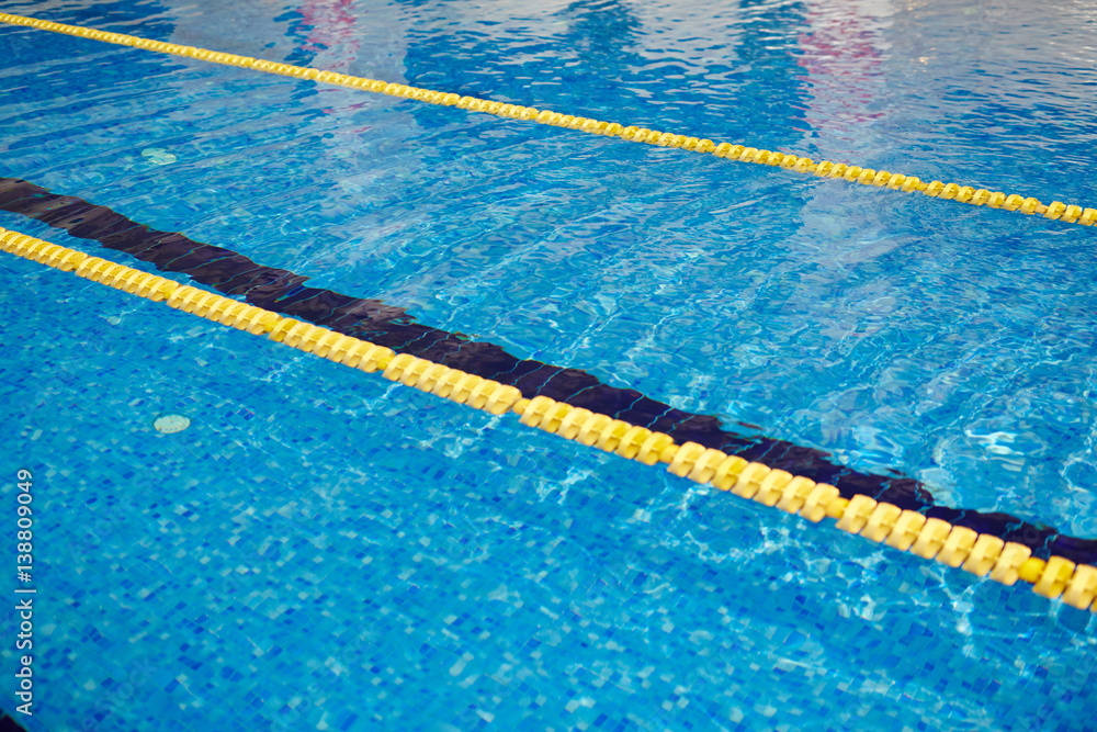 Background image of rippling clear blue water in swimming pool with yellow line on surface