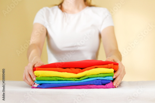 Girl hold on a stack of ironed colored linen. Pile of clothes. Ironing concept. All colors of the rainbow
