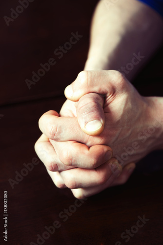 Man's strong hands clasped on dark wooden table