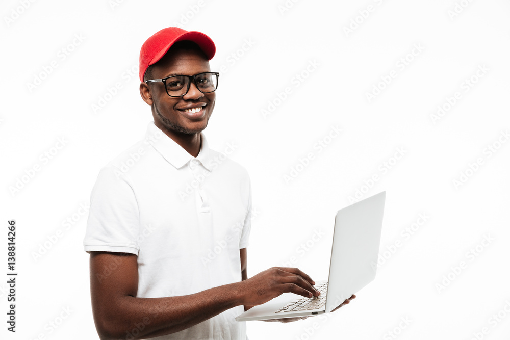 Happy young african man wearing cap using laptop computer Happy young african man wearing cap using laptop computer