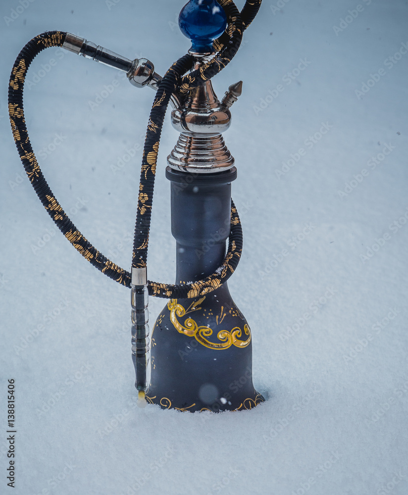 Big hookah for tobacco made of metal, glass and ceramics. Snowing. Snow  background. White Stock Photo