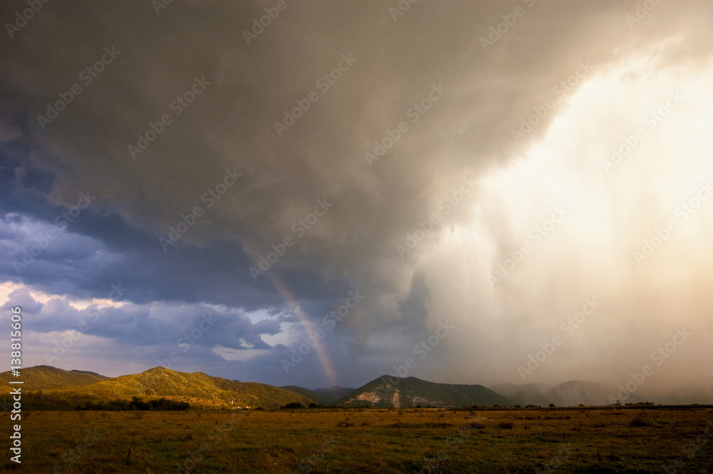 Dramatic sky with storm clouds rain and rainbow at sunset, extreme weather landscape