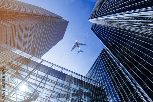 Fotografie Airplane flying over business skyscrapers.