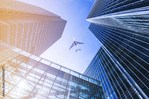 Fotografia Airplane flying over business skyscrapers.