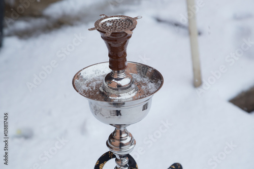 Big hookah for tobacco made of metal, glass and ceramics. Snowing. Snow background. White photo