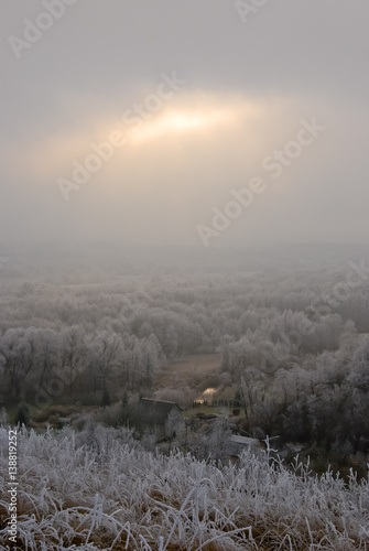Winter landscape with sun shining through clouds and noarfrost covered trees