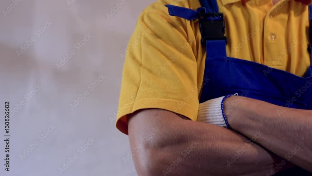 Male repairman in blue coveralls showing thumbs up and crossing arms on