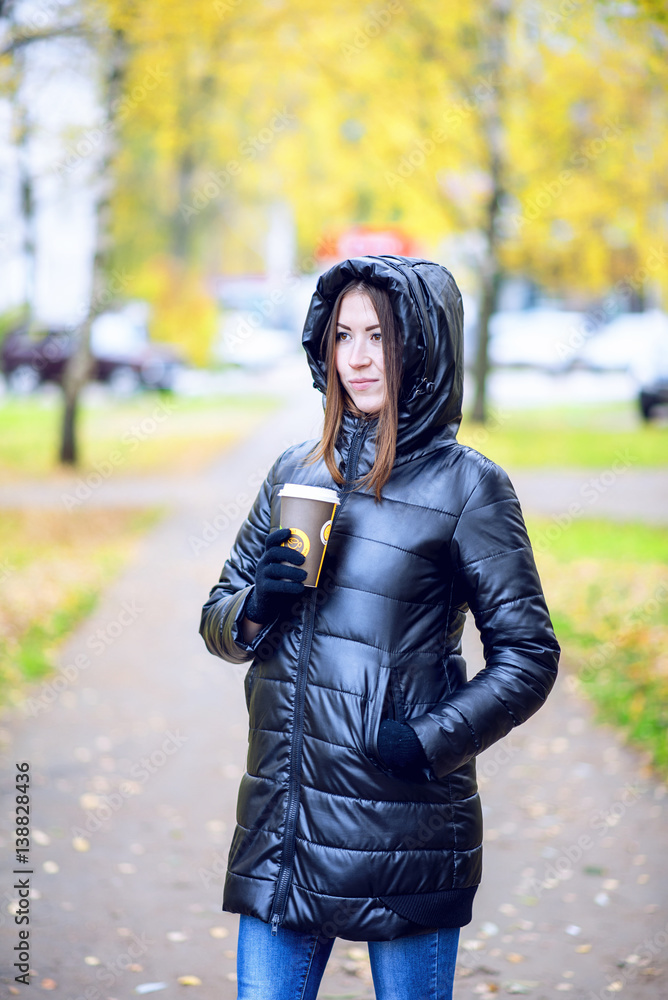 Girl in autumn or spring in a black jacket with a coffee or tea in hand, outdoor. Resting in the city. Life style. Business woman in the hood. Girl in autumn or spring in a black jacket with a coffee or tea in hand, outdoor. Resting in the city. Life style. Business woman in the hood.