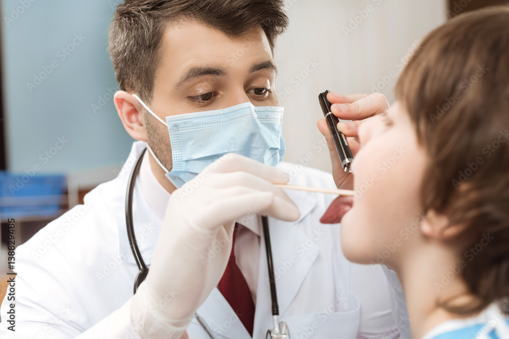 doctor in protective mask examining throat of child patient