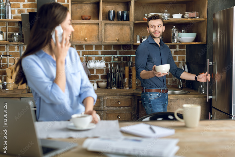 Happy young woman with smartphone and coffee cup looking at man with bowl Happy young woman with smartphone and coffee cup looking at man with bowl