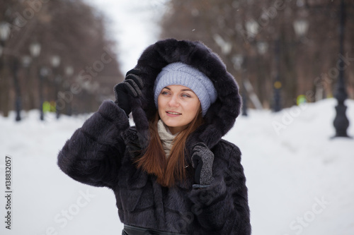 young beautiful girl in a fur coat on a walk in a winter park