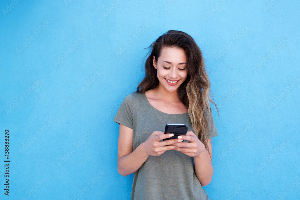 young smiling woman using mobile phone against blue background - obrazy, fototapety, plakaty 
