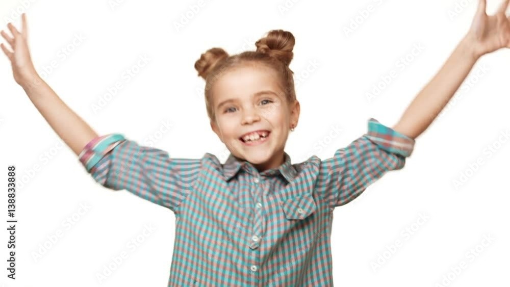Beautiful charming young Caucasian girl kid in plaid shirt jumping and smiling on white background with hands up in slowmotion Beautiful charming young Caucasian girl kid in plaid shirt jumping and smiling on white background with hands up in slowmotion