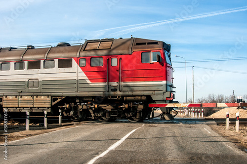 An old russian red train passing across a level crossing, on a small road.
