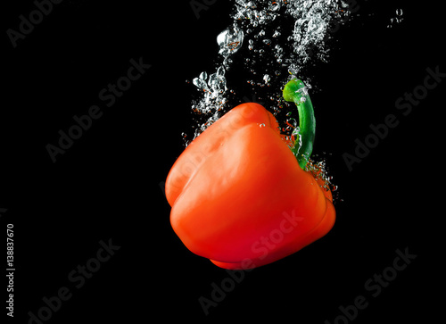 Red paprika pepper falling into the water with a splash and air bubbles. Healthy food on black background. Wash vegetables.