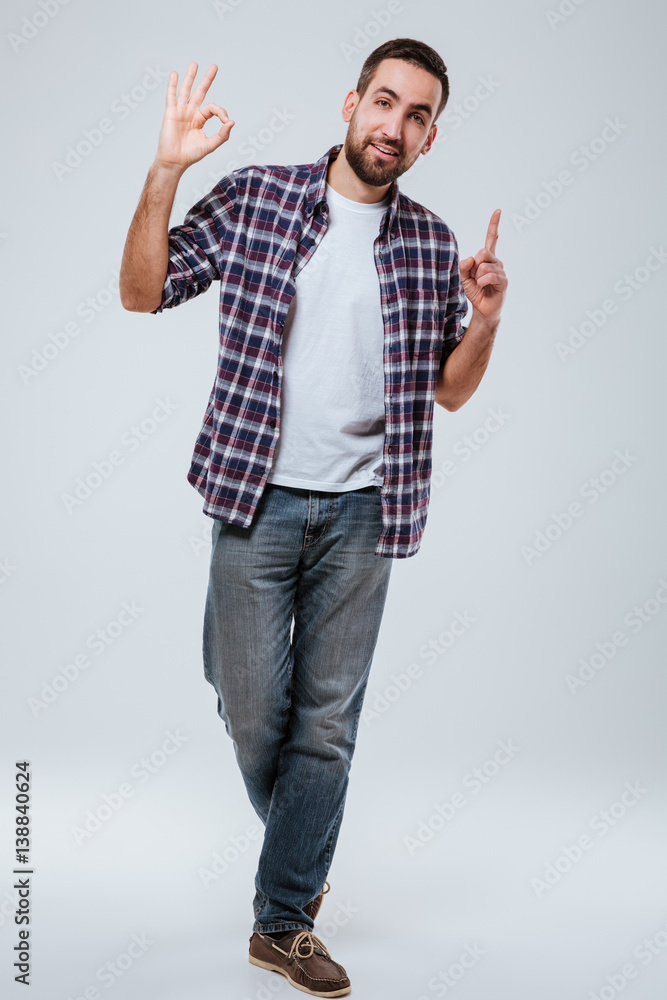 Full length portrait man showing ok sign and pointing up Full length portrait man showing ok sign and pointing up