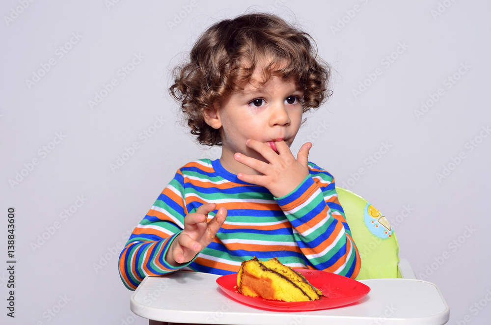 Kid getting messy while eating a chocolate cake. Beautiful curly hair boy eating sweets. Toddler in high chair being hungry. Kid getting messy while eating a chocolate cake. Beautiful curly hair boy eating sweets. Toddler in high chair being hungry.