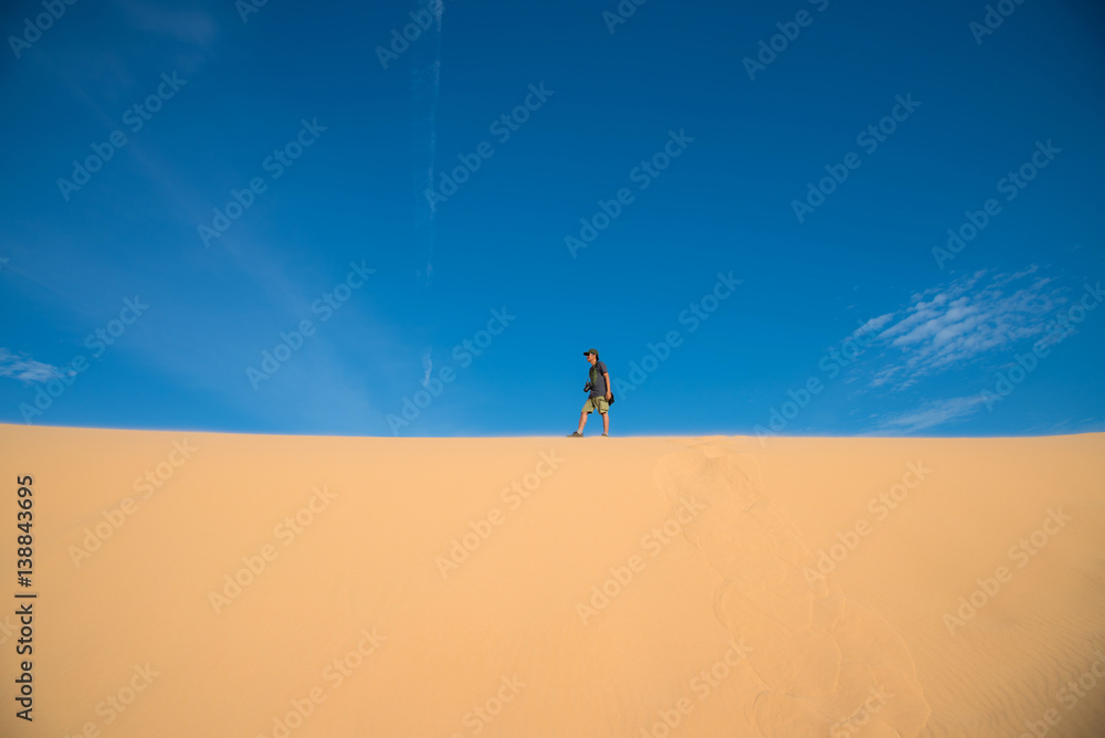 A man walking on white sand dune and blue sky in Mui Ne city, Vietnam