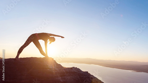 Young woman with yoga posture on the mountain at sunset.