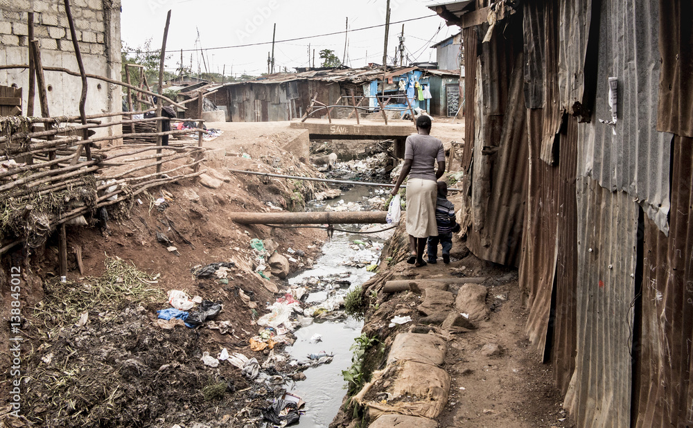 Fototapeta premium Ludzie chodzą po otwartym kanale w slumsach w Afryce