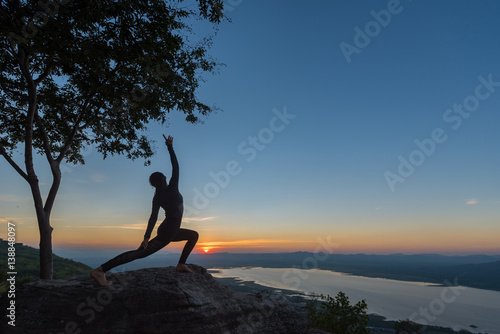Woman with yoga posture on the mountain at sunset.