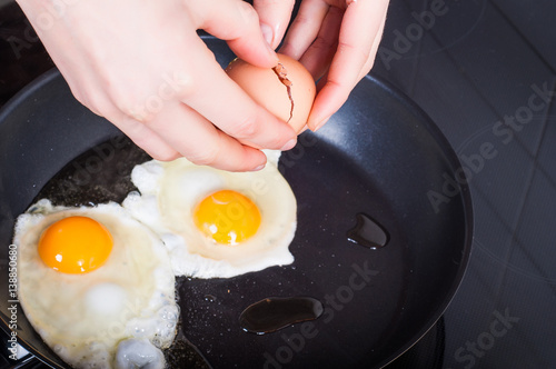 Woman's hands breaking breaking eggs into frying for Sunday's breakfast. Healthy eating concept